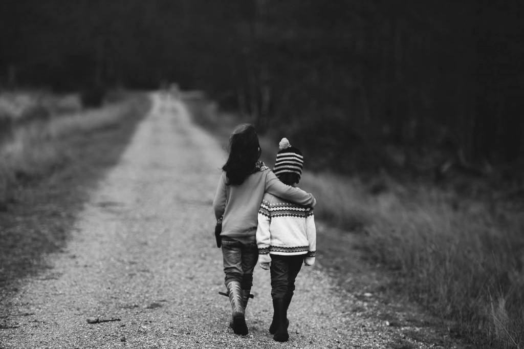 A black and white pictures of siblings walking down a trail. 