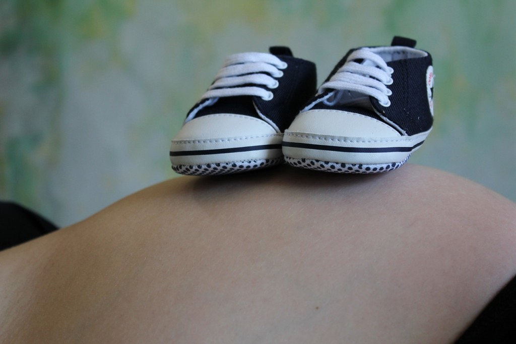A woman's pregnant belly has two little Converse shoes on top. 