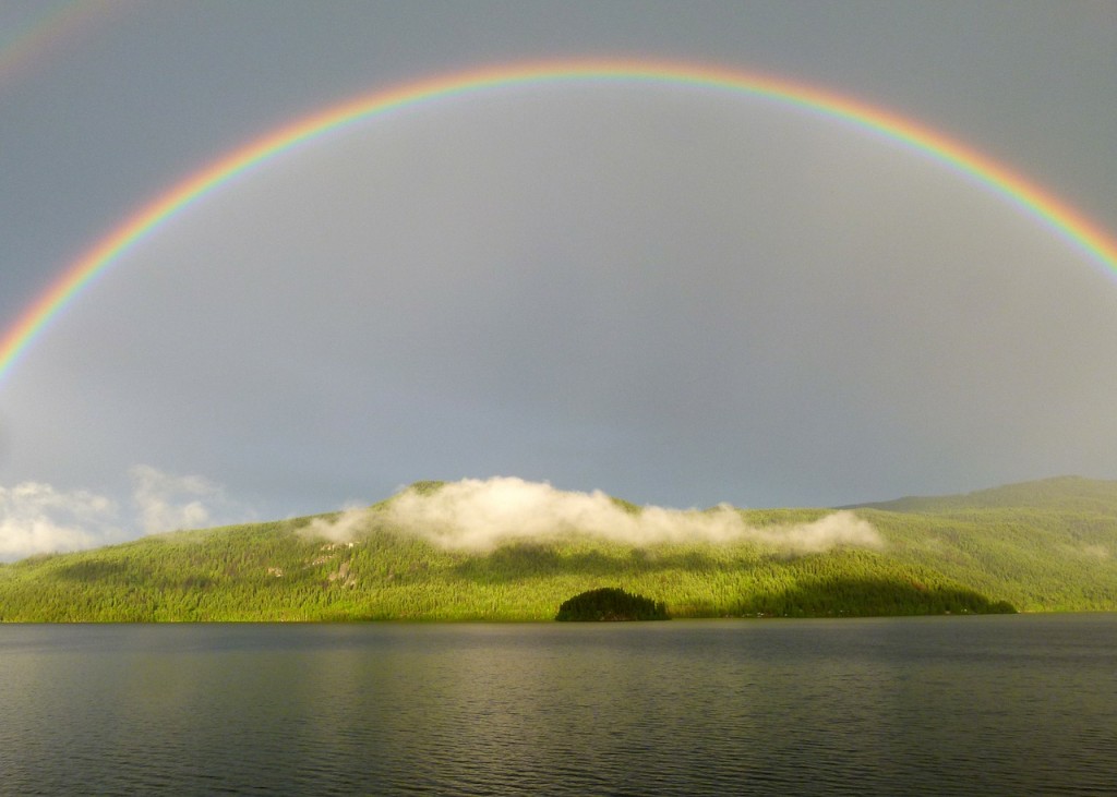 Hey all. A rainbow in the sky over a hill and water. 