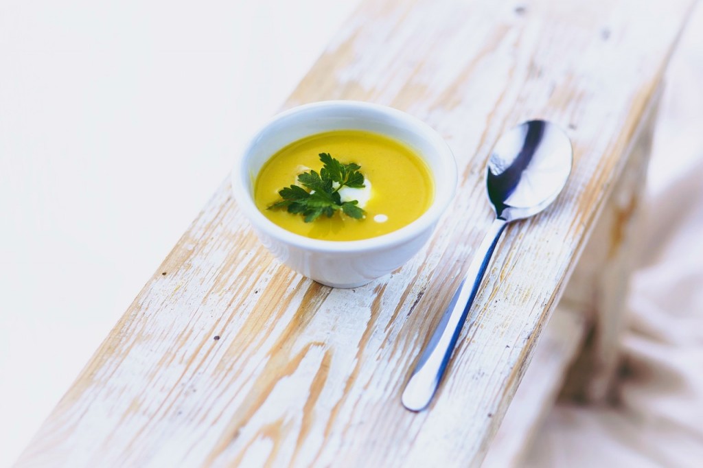 A piece of wood acts as a table for a soup filled with squash soup, herbs, sour cream and a spoon next to it. 