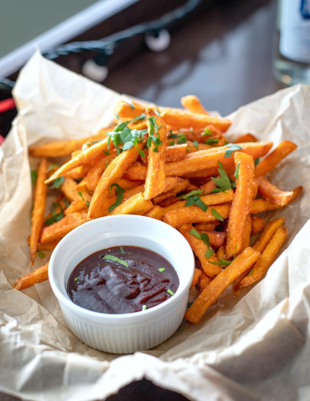 A plate full of sweet potato fries topped with herbs and bbq sauce to dip. 