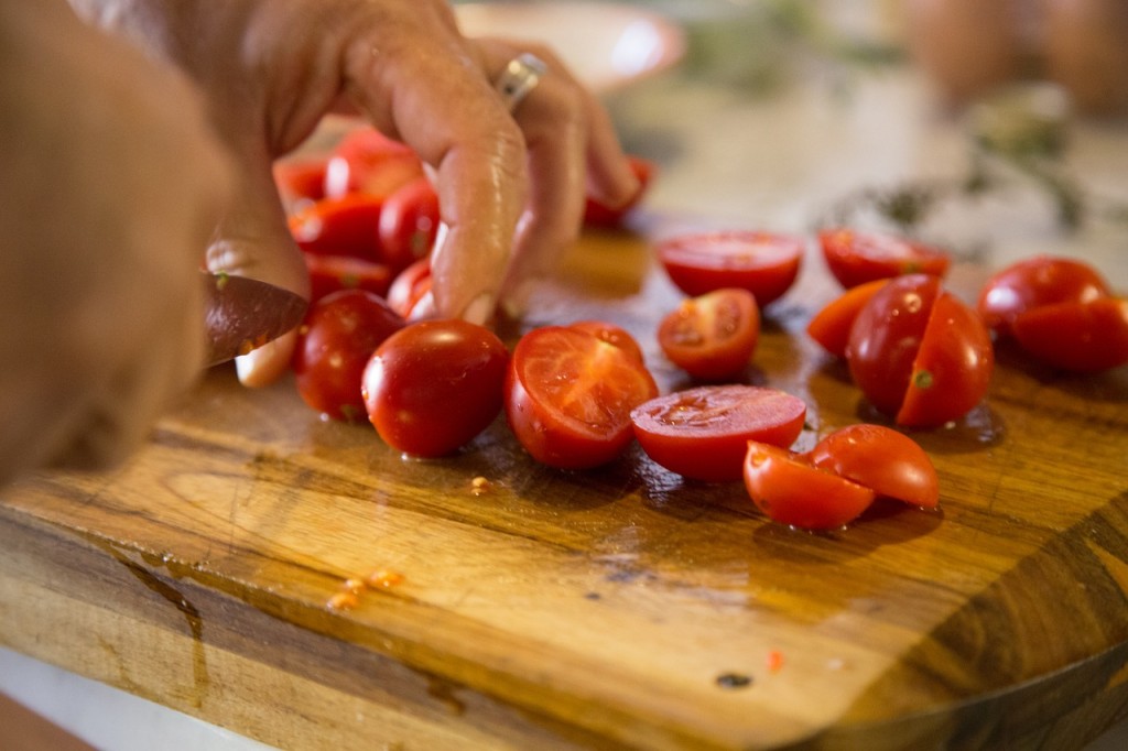 A woman is dicing tomatoes on a wooden board.
