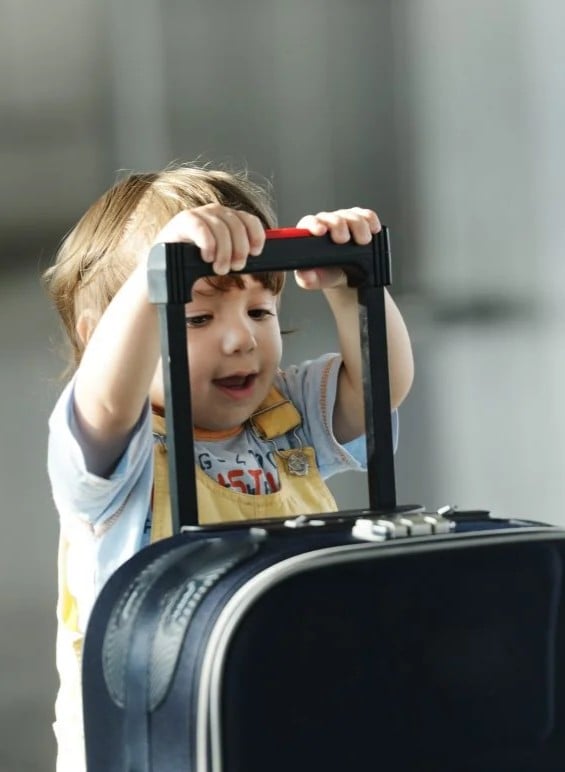 A little baby holds onto a carry-on and smiles. This article shares tips for traveling with a baby.