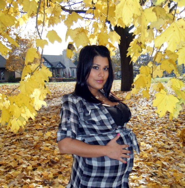 A woman hold her pregnant belly with love against fall foliage. 