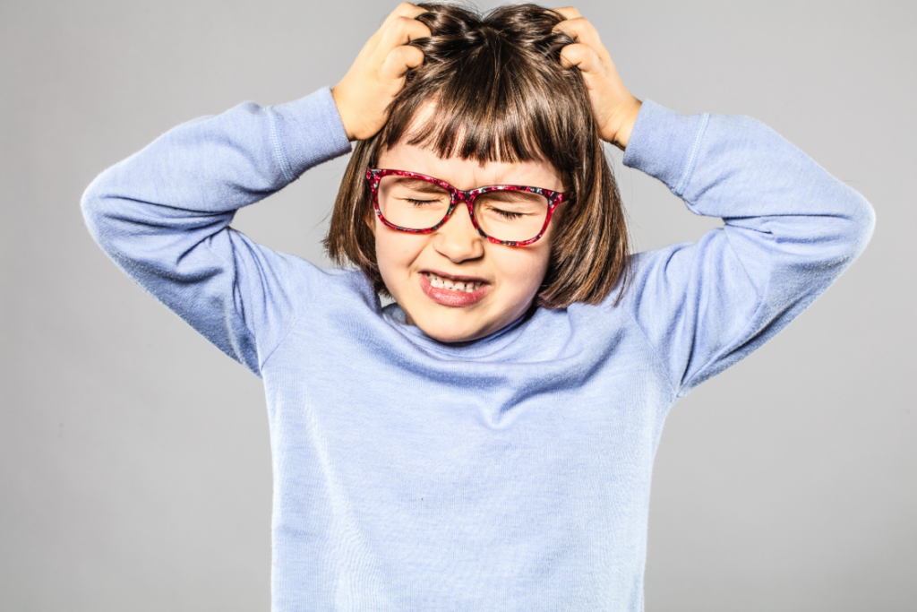 A little girl with glasses winces, closes her eyes, and scratches her head. This article covers 6 Tips on How to Prevent Head Lice.