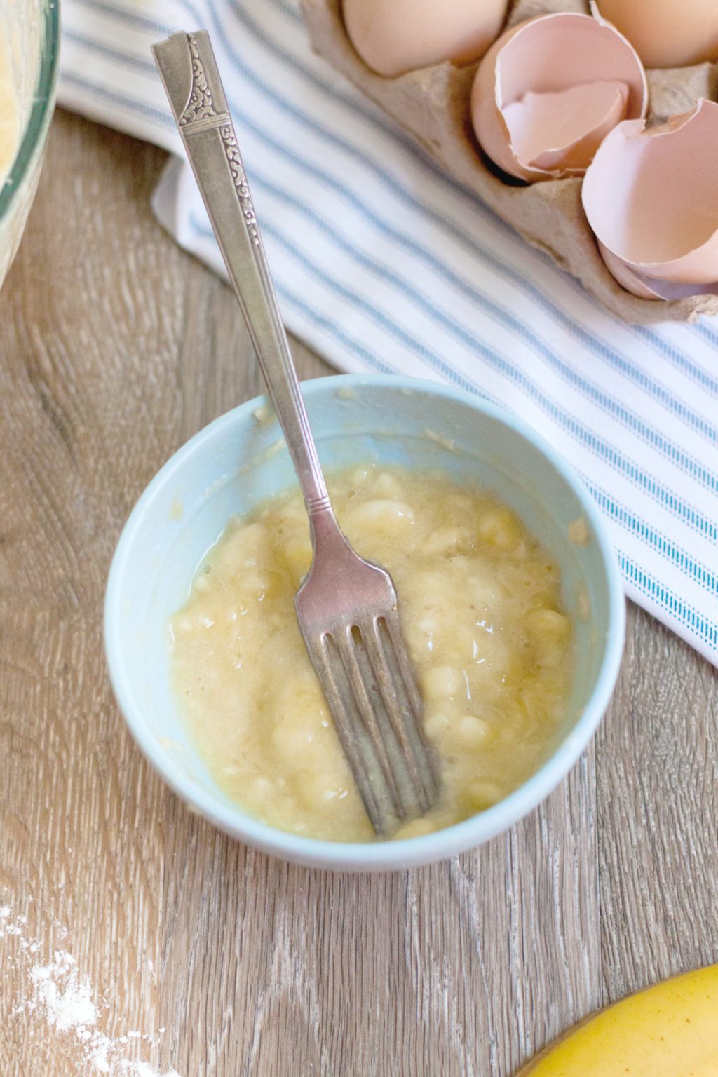 Banana is mashed with a fork in a small bowl.