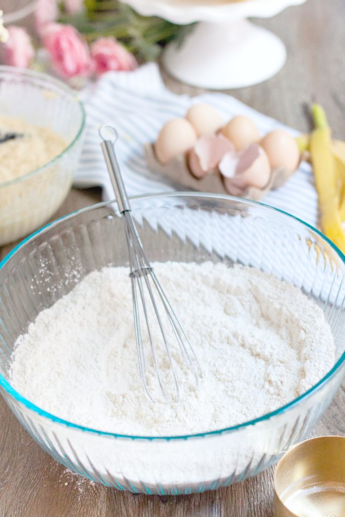 Whisk is shown inside flour and dry mixture in a bowl. 