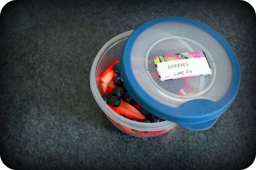 A halfway open tupperware with berries and an label with with an expiry date is on the lid.