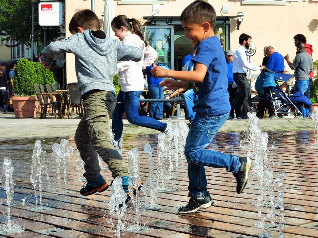 Two little boys run in sprinklers. This article covers 6 Tips to Stay Cool and Safe in The Heat!