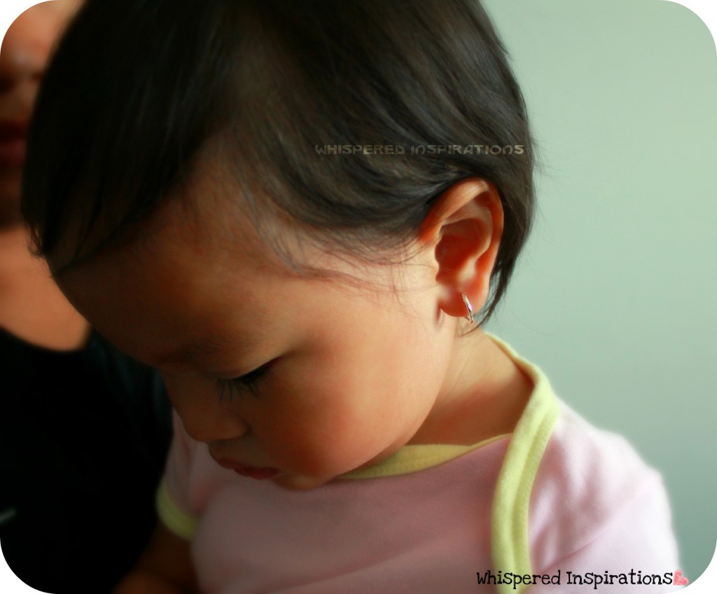 A baby looks down and shows off her hoop earrings. 