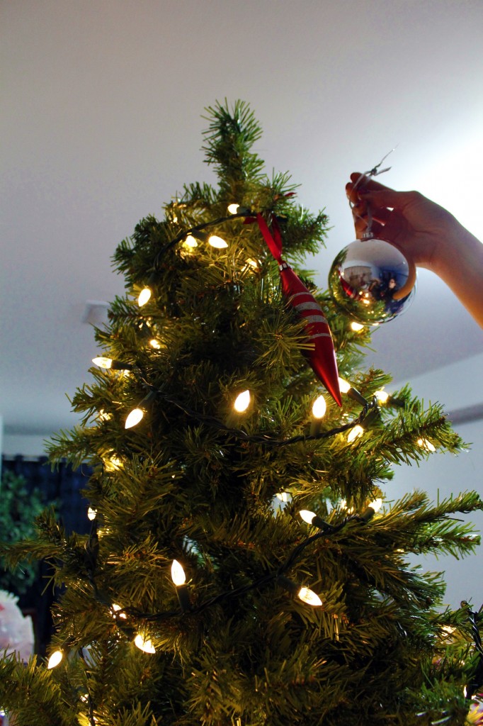 A woman places an ornament at the top of the tree. 