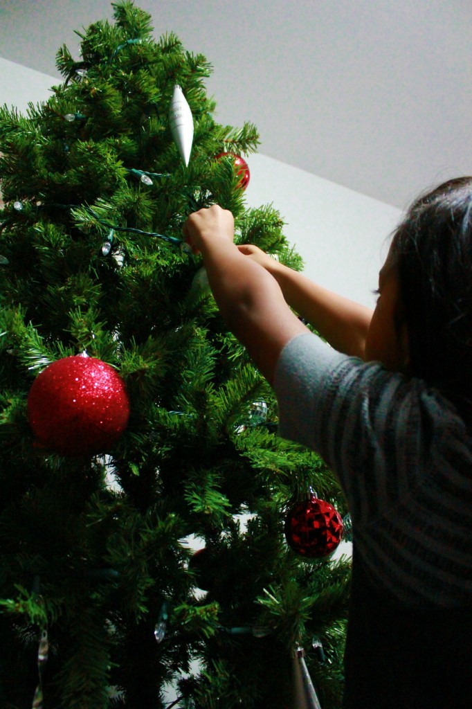 Little girl places ornaments on Christmas tree. 