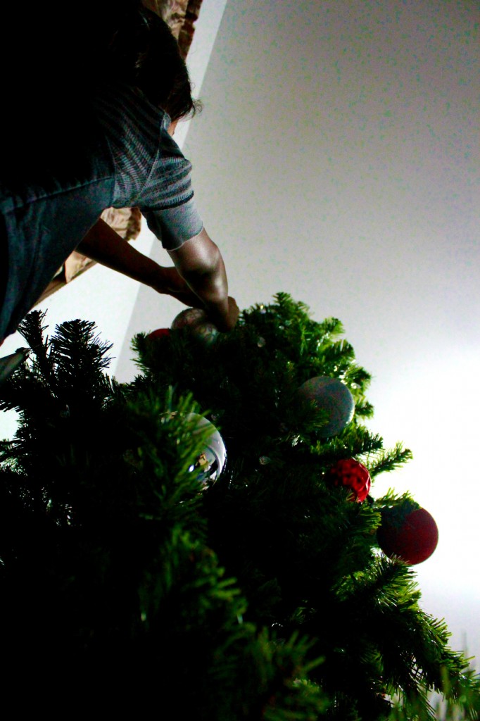 Little girl placing ornaments on tree. 