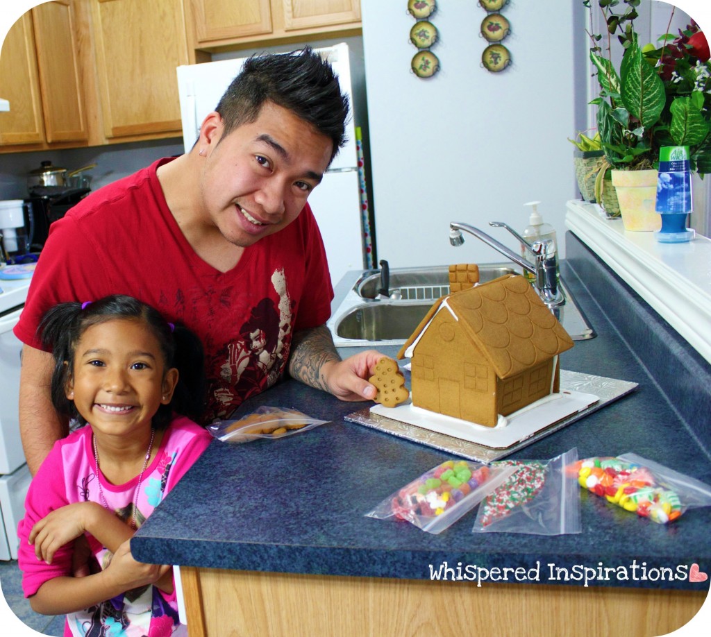 A little girl and her dad make a gingerbread house in the kitchen. 