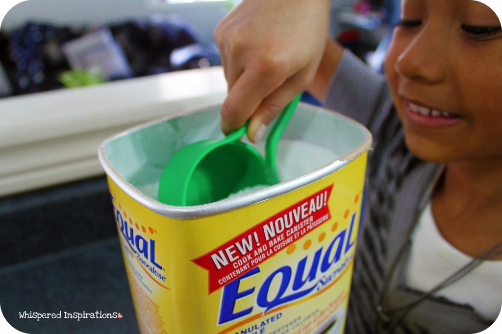 A little girl reaches in to the Equal tub with a measuring cup. 