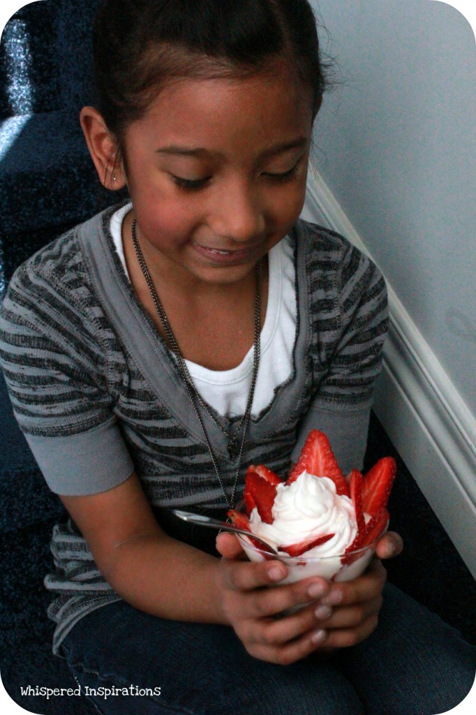 Little girl looks down at a yogurt parfait. 