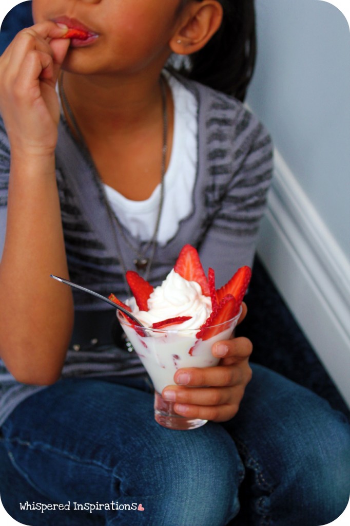 A little girl eats a yogurt parfait with strawberries. 