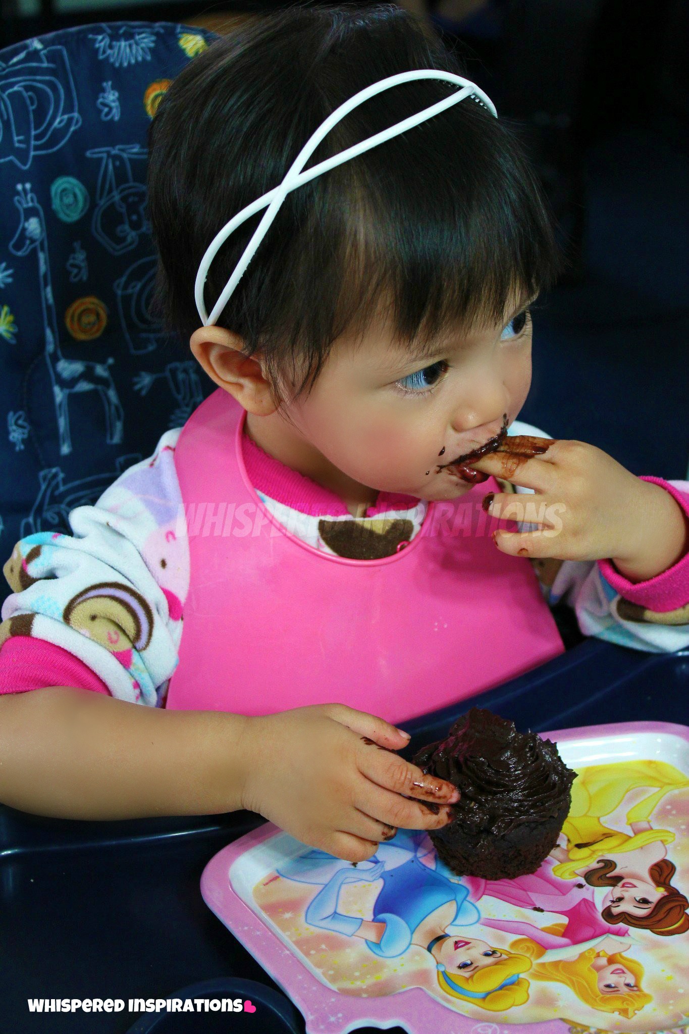 Mimi, a little girl, licking her little fingers while eating a chocolate cupcake.
