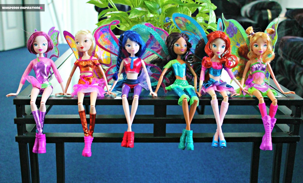 Six Winx Dolls sit on the edge of a coffee table. 