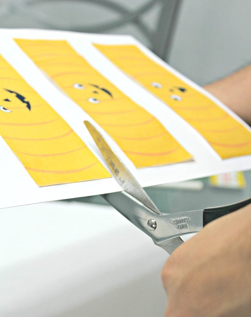 A hand is shown cutting the printable after it's been pasted onto thick paper.