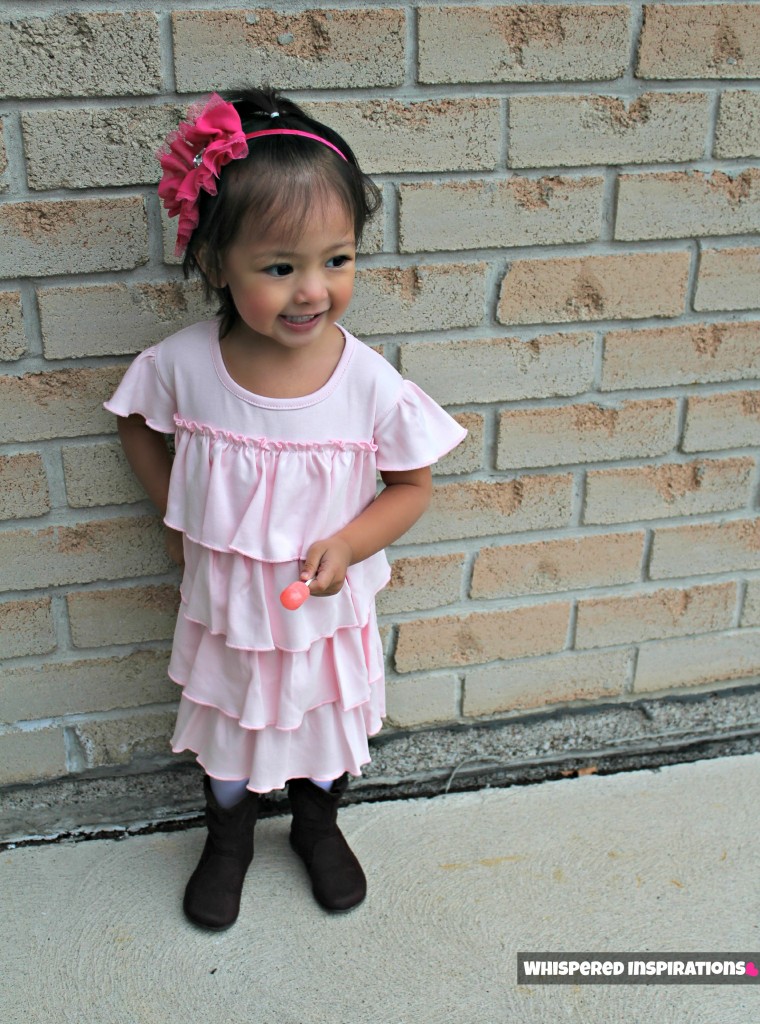 Little girl stands outside posing in front of a brick wall and shows off her dress. 