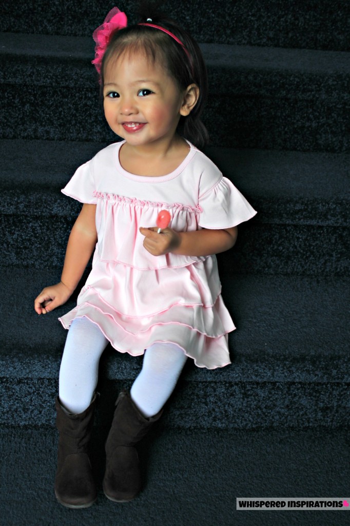 Little girl sits on the stairs while holding a lollipop and smiling. 