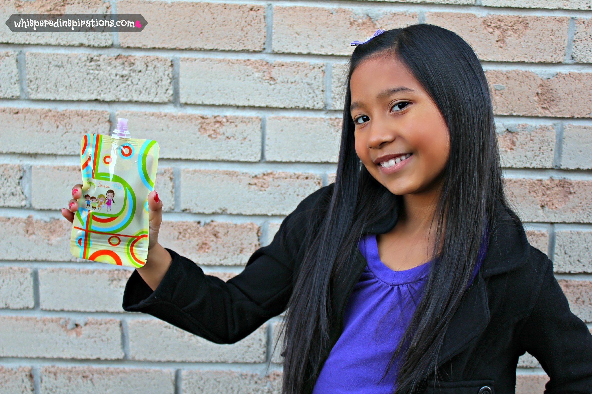 A little girl holds up a Squshy Snak Pack and smiles. 