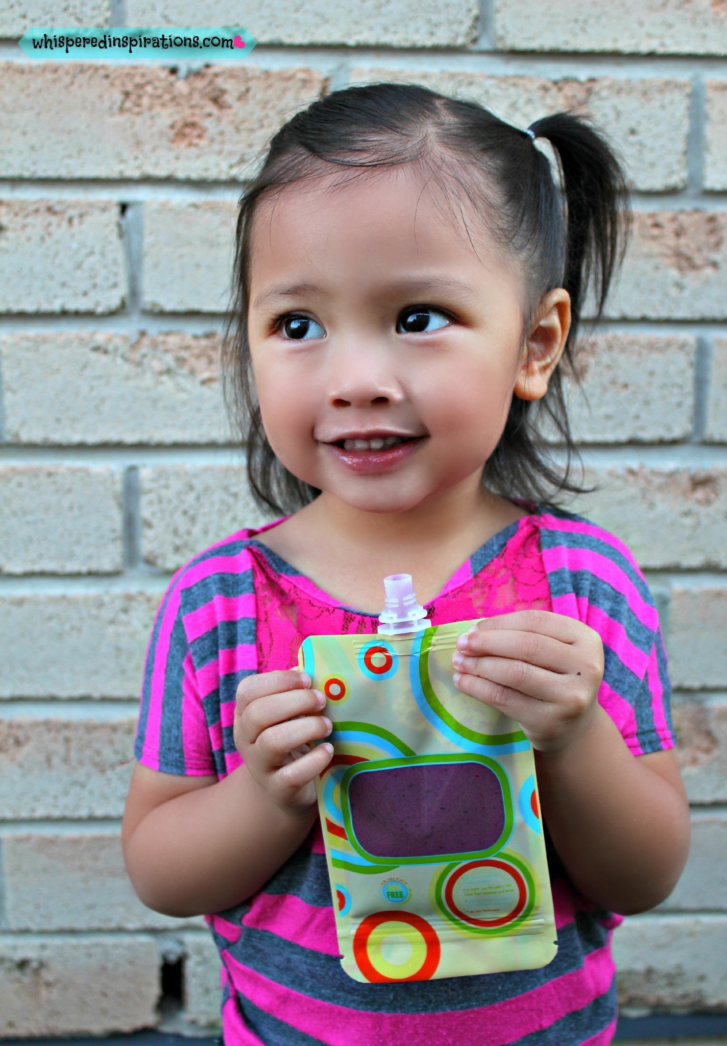 A little girl enjoys fresh fruit in a Squishy Snak Pack.