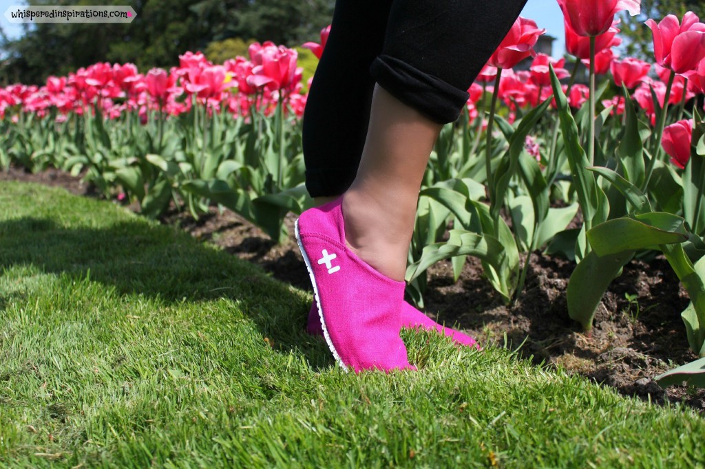 Nancy stands in front of pink tulips posing with OTZ shoes in hot pink.