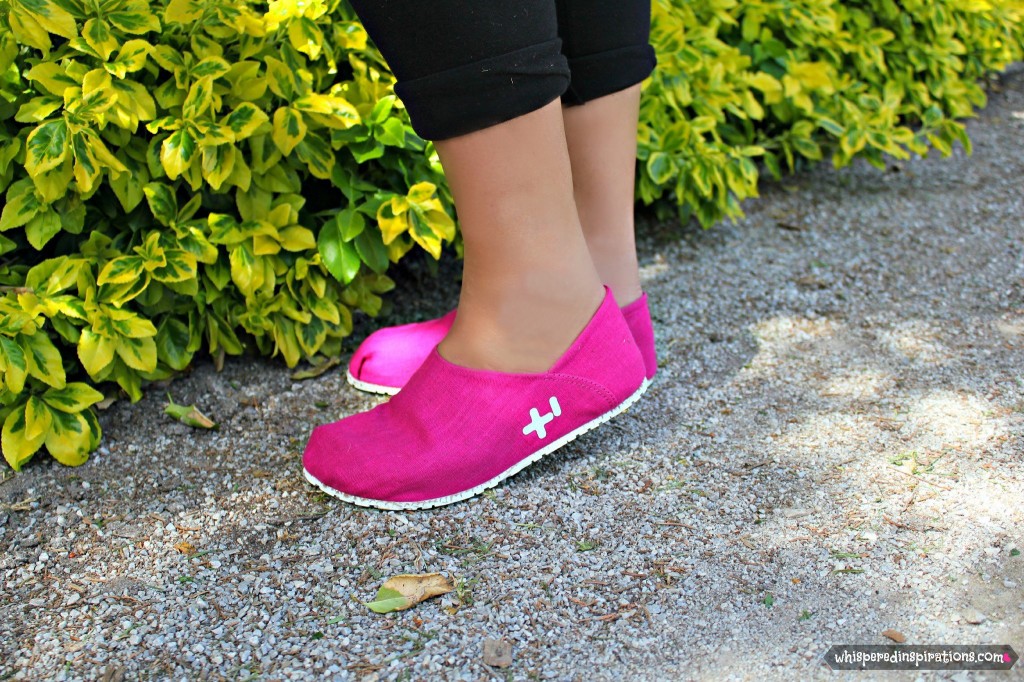 The OTZ shoes are worn by Nancy, she is standing in front of vibrant green bushes.