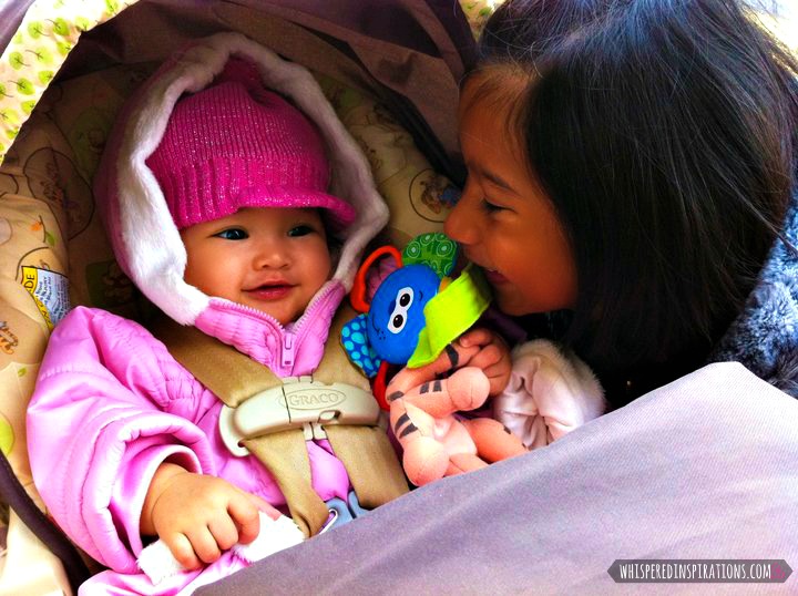 A little girl looks at her sister in her car seat.
