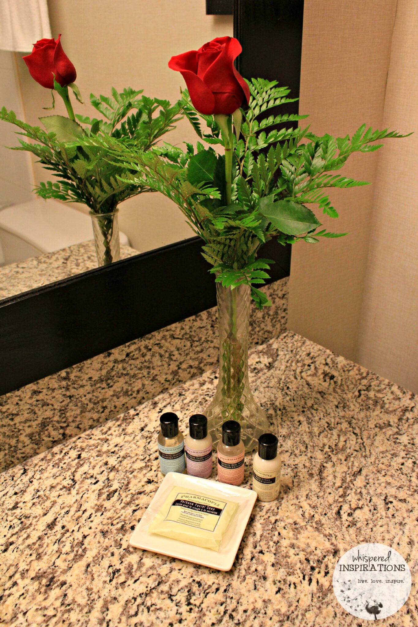 A vase with roses in the washroom with toiletries.