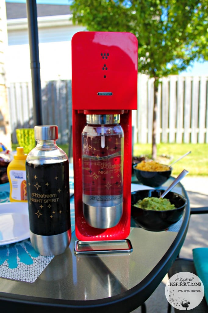 Red SodaStream is on a patio table. Rice and guacamole with a bottle of prepared soda are shown. 