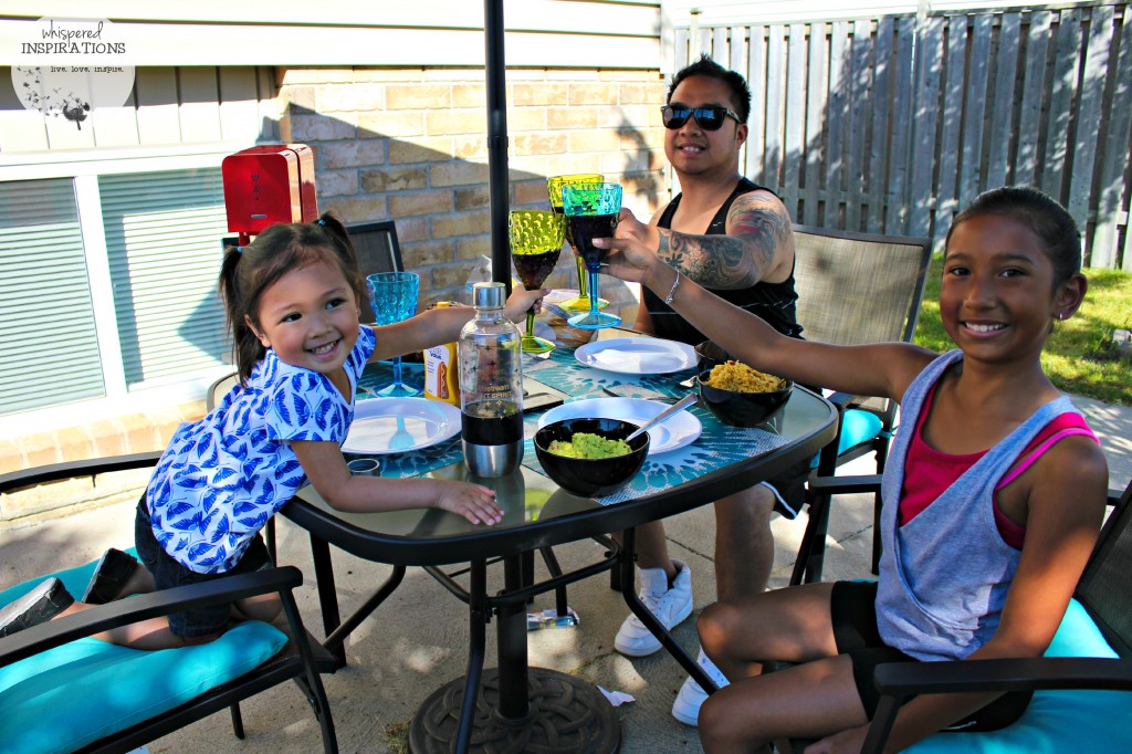 Two girls with their father cheer with SodaStream soda in their backyard patio.