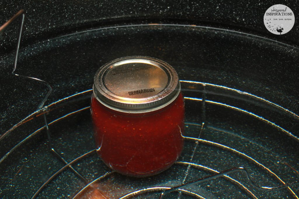 Mason jars filled with the organic strawberry and blueberry jam recipe are submerged to be sealed. 