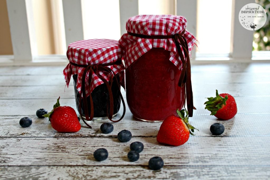 Two jars of homemade jam are wrapped with plaid and surrounded by strawberries and blueberries. Made with Bernardin Home Canning. 