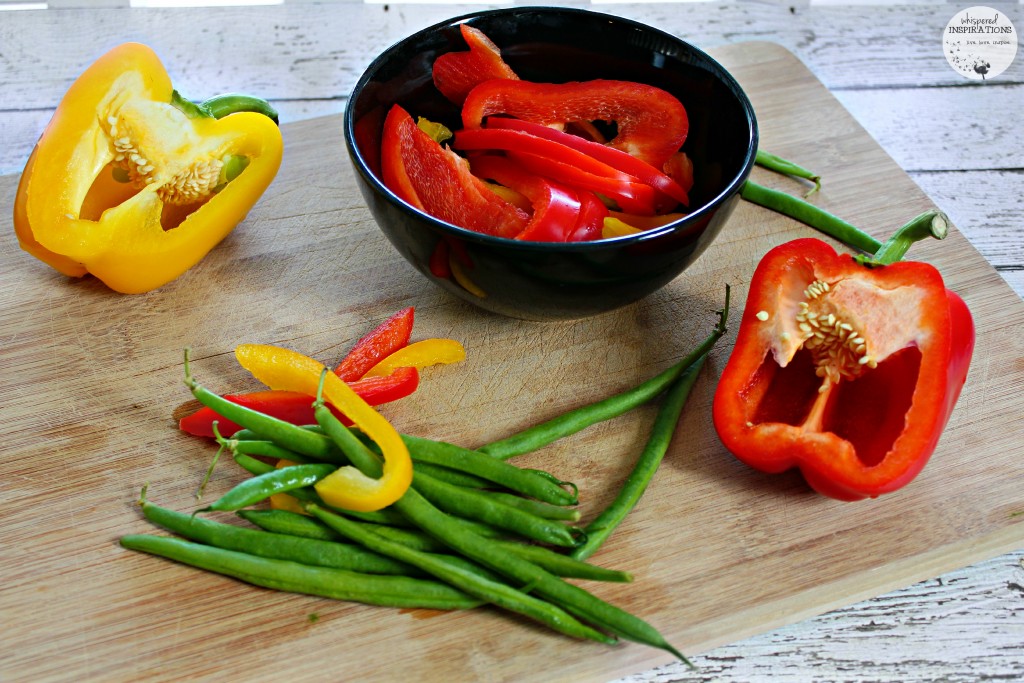 Red and yellow pepper are cute and green beans are strewn on a cutting board. 