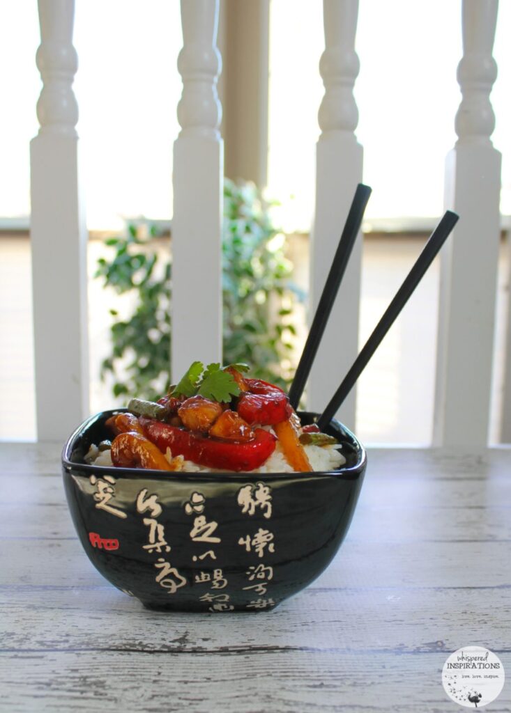 A bowl with rice and Sesame Chicken Stir-Fry and chop sticks. 