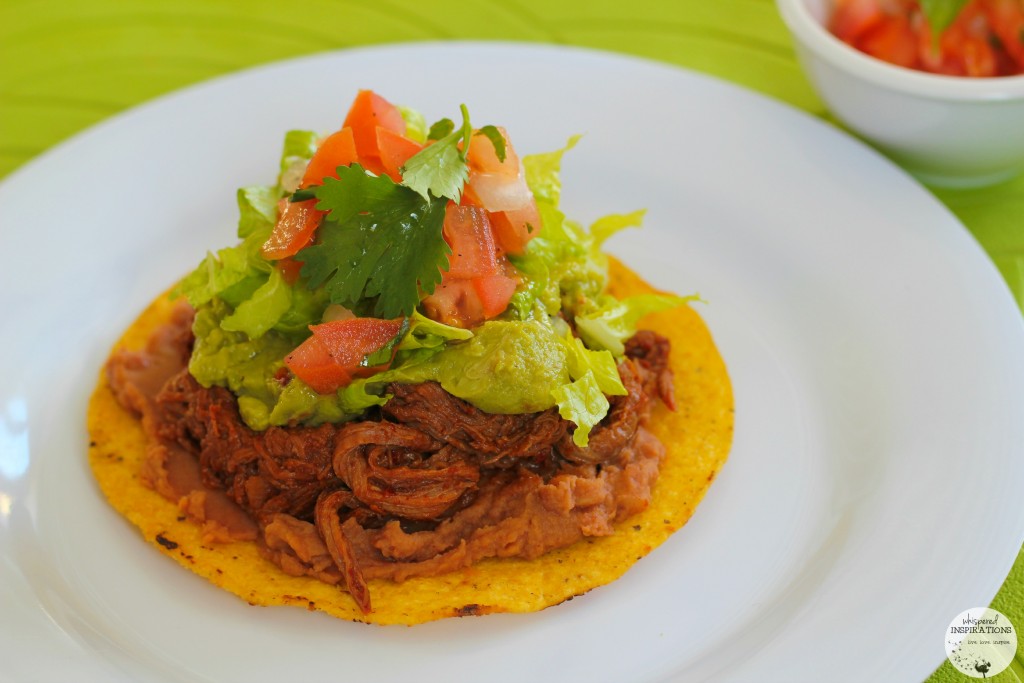 A Salvadorean Beef Enchilada topped with refried beans, shredded beef, guacamole, pico de gallo, and lettuce.