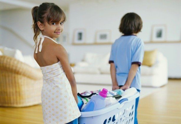 Girl (6-8) carrying basket of laundry with brother (5-7) smiling