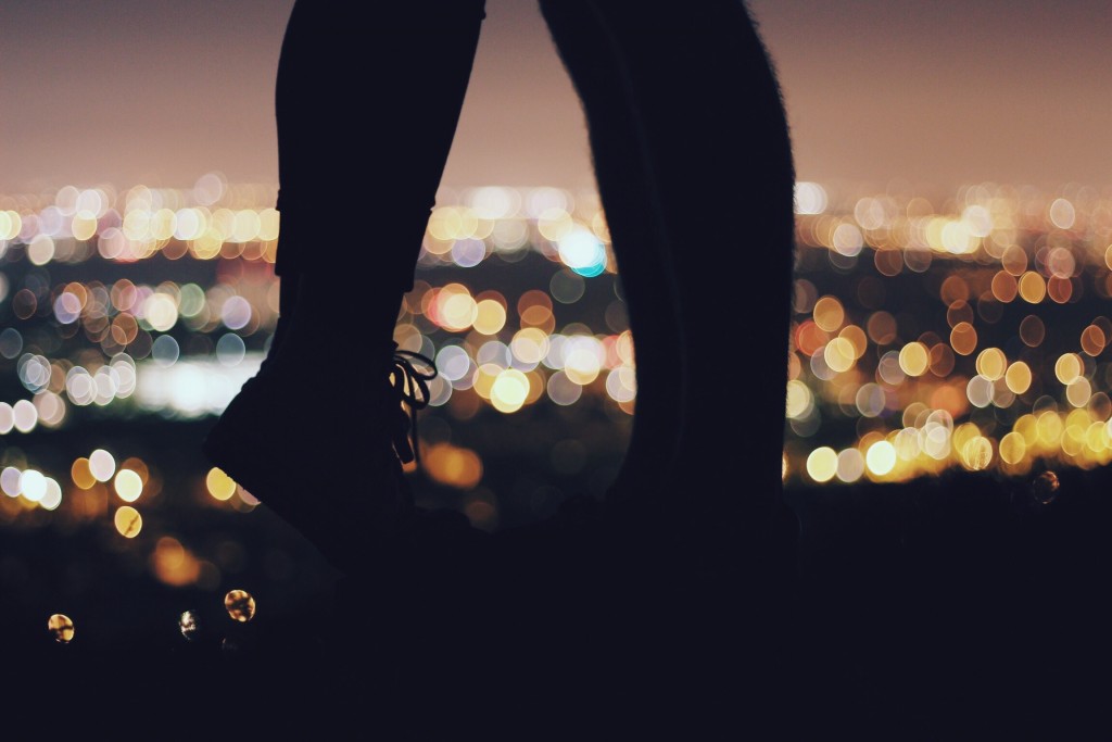 A couples' feet are shown and the girl is on her toes, the city lights are in the background.