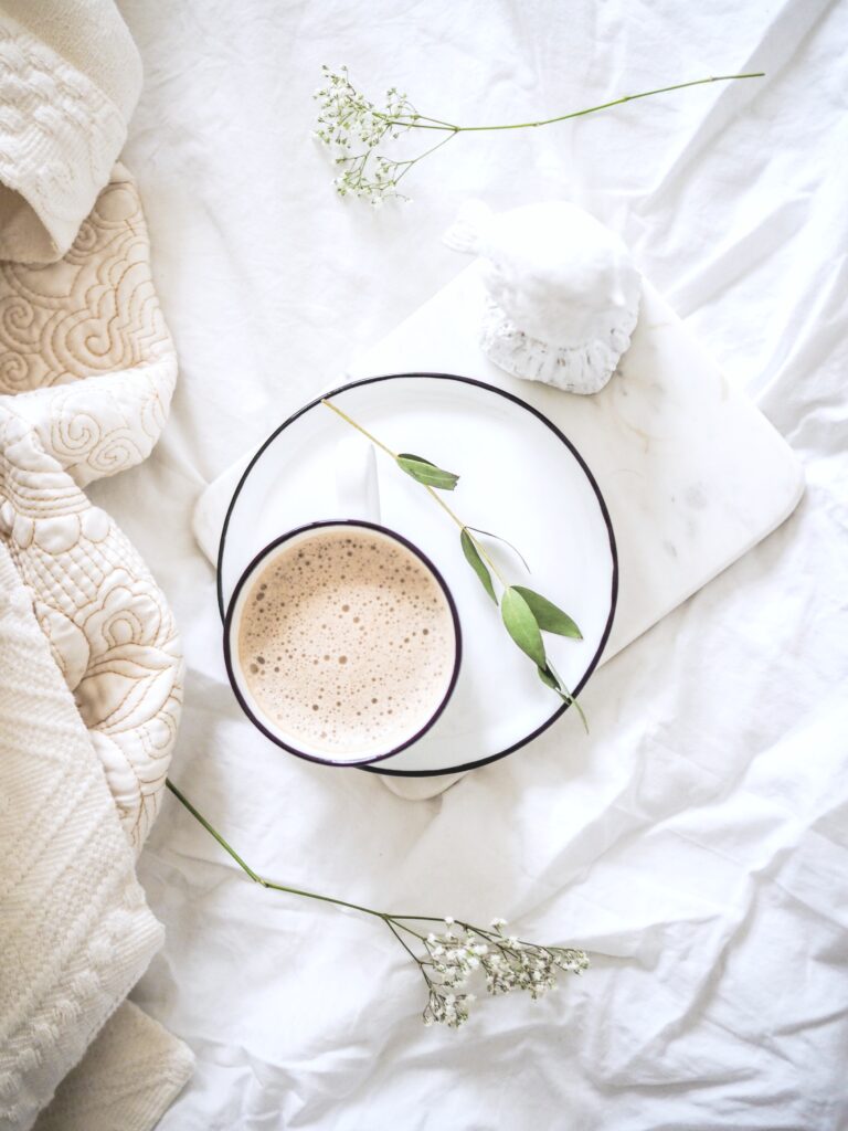 Bed with latte and plate, white sheets, and a blanket.