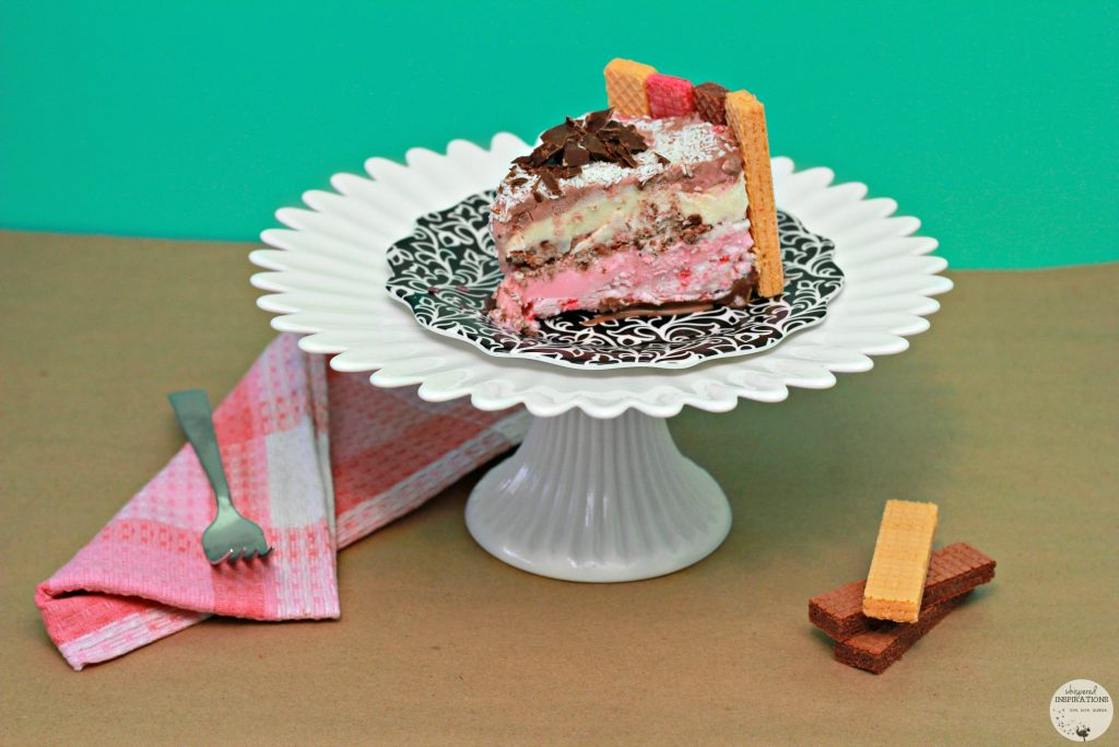 A slice of Neapolitan Ice Cream Cake Inspired by Voortman on a cake holder and plate. 