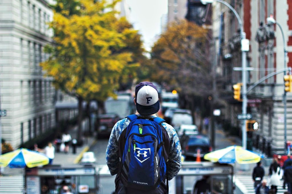 A boy stands in a big city and looks out, he has a back pack on. He is a student. This article covers student loan debt.