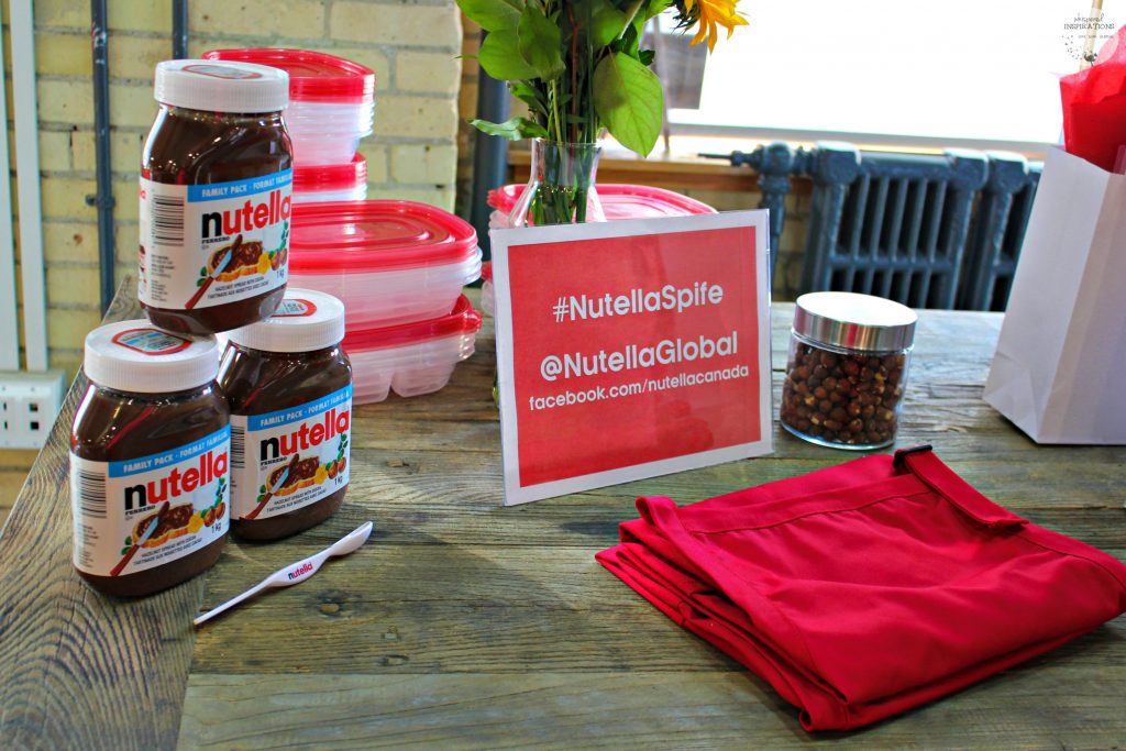 Nutella jars, Nutella spife, and aprons on a table.