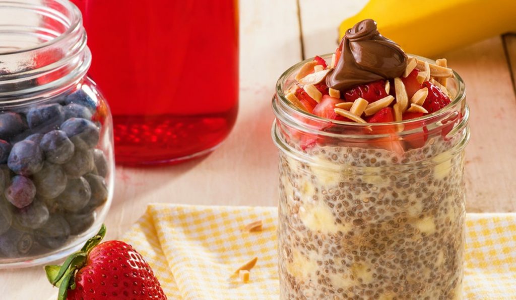 Mason jar filled with chia pudding, strawberries, slivered almonds, and Nutella. 