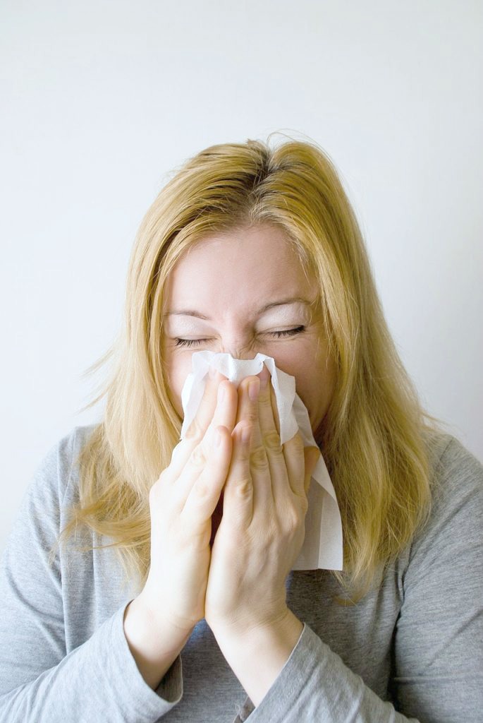 Woman sneezing into a tissue. Her eyes are closed.