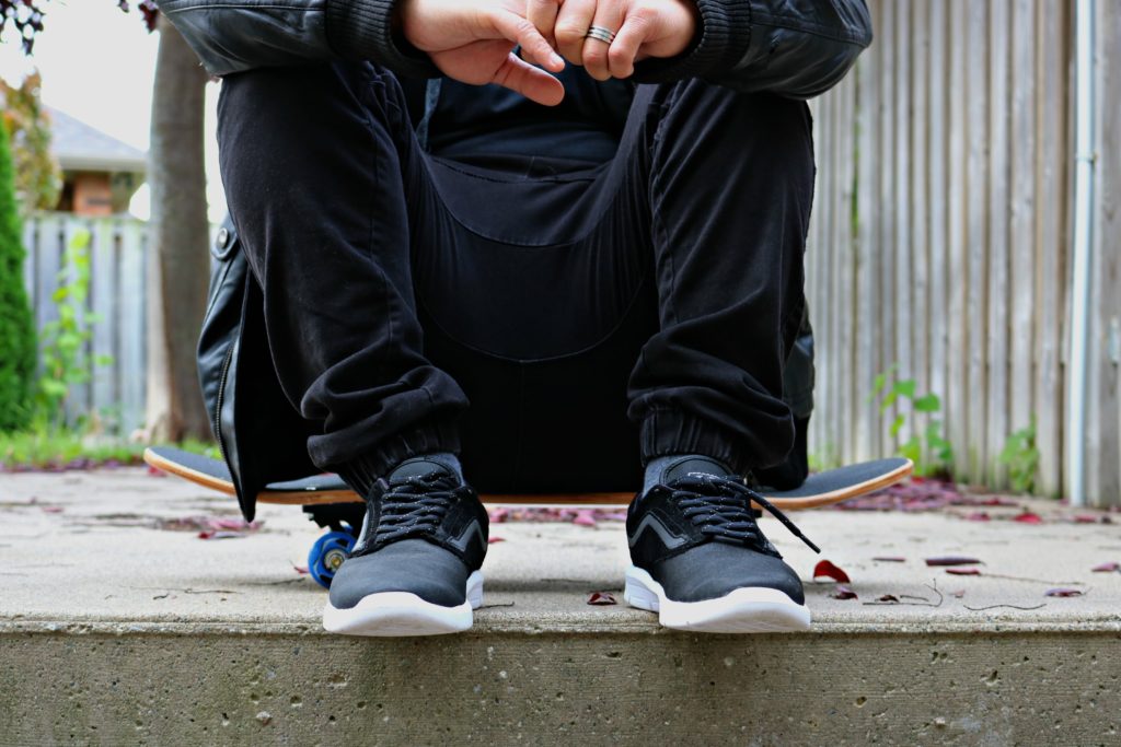 Darasak sits on a skateboard and only his shoes, pants, and hands are shown. 