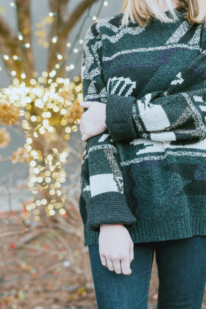 Close up of a woman, face not shown, standing in front of Christmas lights. 