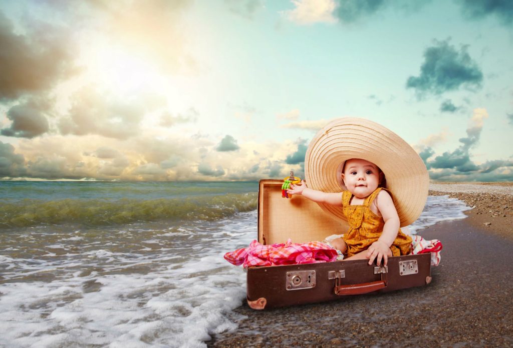 Baby wearing a hat sits in suitcase, that washed up on the beach. This article covers tips for traveling with baby for the first time.